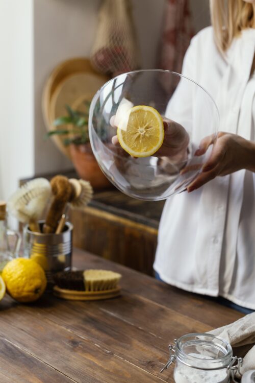 Femme tenant un saladier en verre parfaitement propre avec une tranche de citron visible à travers, illustrant l'efficacité du nettoyage naturel en cuisine.