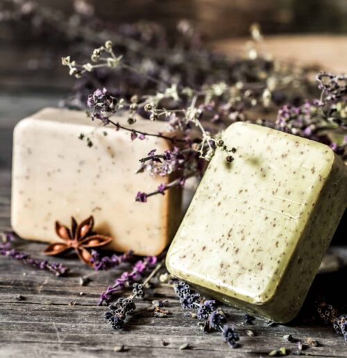 Deux savons artisanaux exfoliants sur un fond en bois avec de la lavande séchée, illustrant la fabrication de produits écologiques pour les sanitaires.