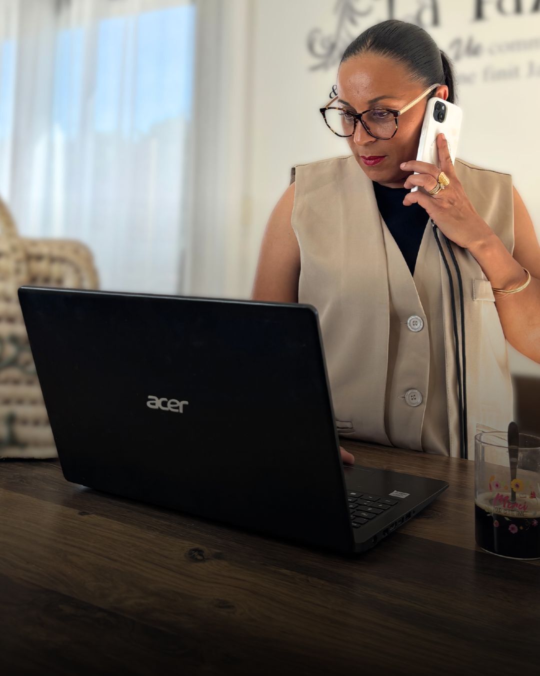 Portrait professionnel de la directrice de la Soussou Academy, portant un gilet beige et des lunettes, en pleine conversation téléphonique tout en travaillant sur un ordinateur portable Acer, illustrant le service d'accompagnement et de suivi des stagiaires.