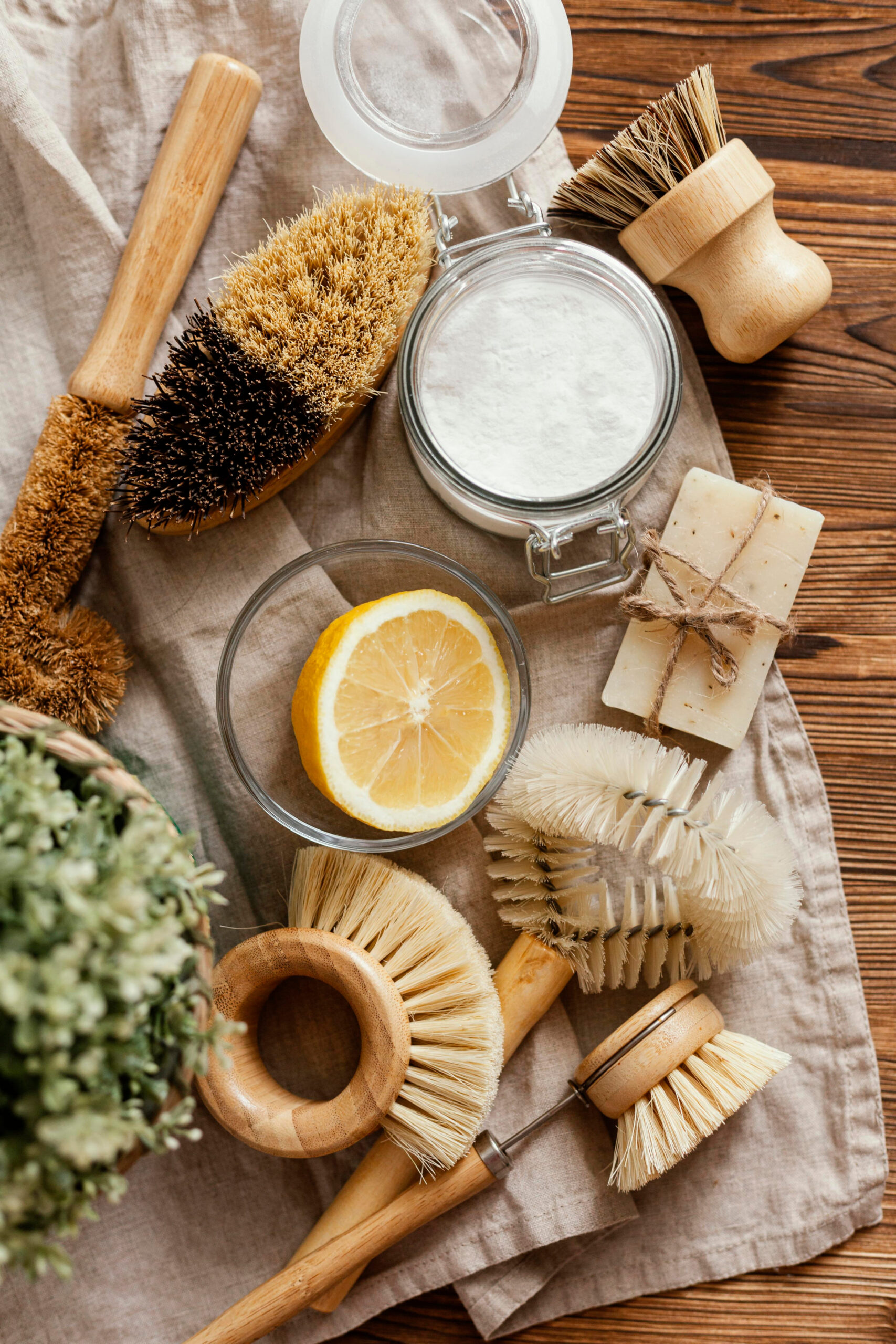 Assortiment d'accessoires de nettoyage naturels : brosses en bois, citron, bicarbonate de soude et savon artisanal sur un linge en lin pour les ateliers Soussou Academy.